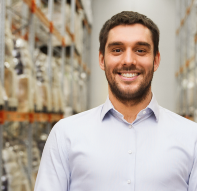 wholesale, logistic, business, export and people concept - happy brunette man in a white shirt with tablet pc computer in a warehouse surrounded by large shelves.