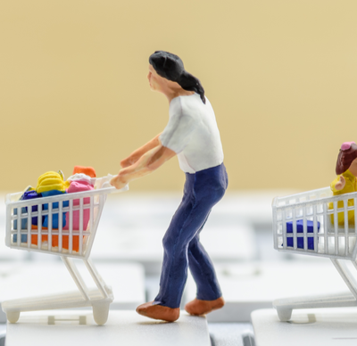 Miniature figurine shopper push a shopping cart on a computer keyboard, depicts buyers or consumers order or buy things from retailer stores over the internet