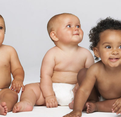 Row of multi-ethnic babies sitting side by side looking away isolated on a grey background