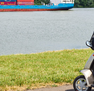 Elderly man sitting in mobility scooter enjoying watching a cargo ship passing by