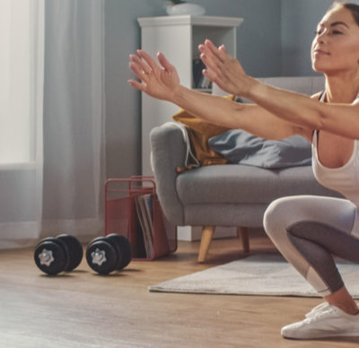 Strong Athletic Fitness woman  in Sportswear is Doing Squat Exercises in Her Bright and Spacious Living Room with Minimalistic Interior.