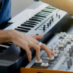 music producer is composing a song on synthesizer keyboard and computer in recording studio. Man is working on sound mixer in recording studio or DJ is working in broadcasting studio