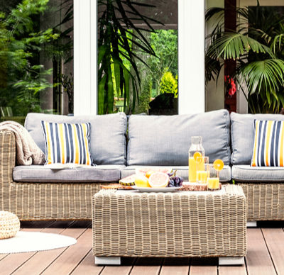 Outdoor rattan furniture. A relaxing spot for a warm, summer day - a stylish, wooden terrace with wicker garden furniture, cushions, plants and flowers