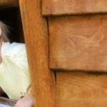 Curious toddler boy, peering from a small window in wooden shed like building, making a funny face
