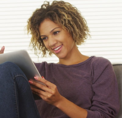 Happy woman sitting on a grey sofa using a tablet in lounge