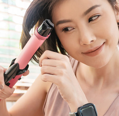 Portrait of young woman curling her hair with ceramic curler straightener home smart object electronic device