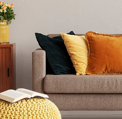 Abstract painting on grey wall of retro living room interior with beige sofa with pillows, vintage dark green armchair and yellow pouffe with a book