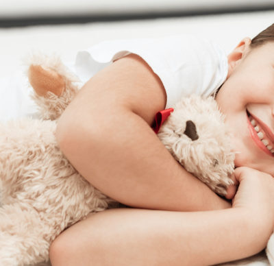 Smiling little girl hugging teddy bears lies on mattress.
