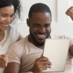 Excited happy family couple looking at digital tablet celebrating getting a good deal